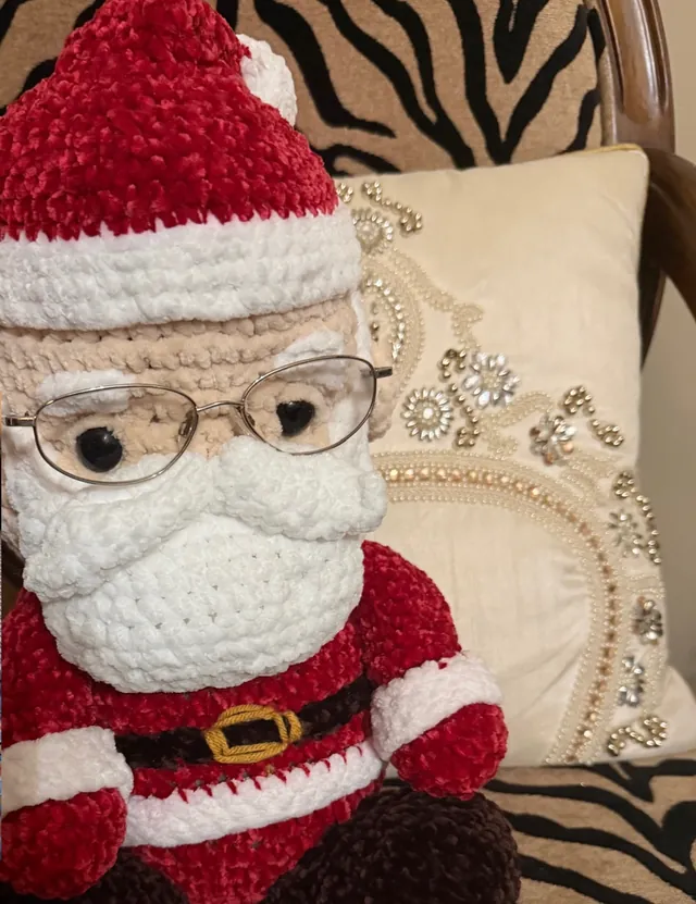 Close-up of a crocheted velvet Santa with a fluffy white beard and real wire-rimmed glasses