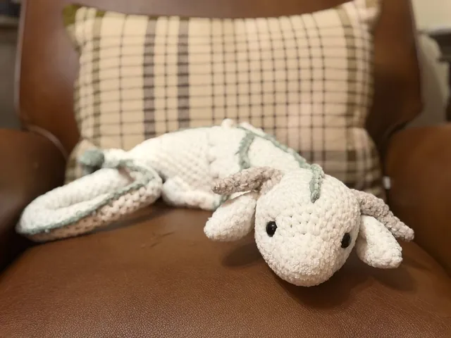 A long cream chenille dragon with a sage-green spine and small curled horns, lounging on a leather chair